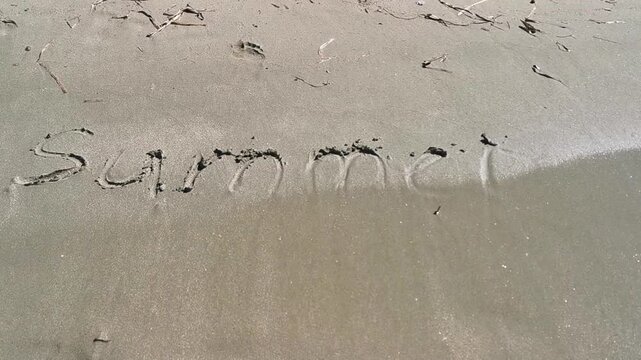 Sand writing of the word "summer" gradually eroded by gentle ocean waves on a sandy beach, showcasing the transition from clear to fading text