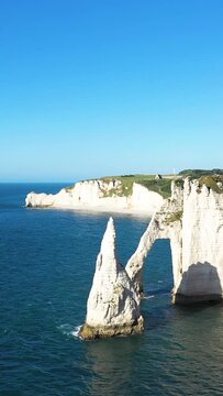 Dramatic white chalk cliffs and natural sea arch rising above the blue waters at Etretat, Normandy, France, under a clear sky.