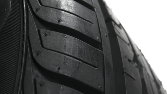 Grippy Tread of a New Tire. Car wheel slowly rotates in front of the camera close-up on a white background