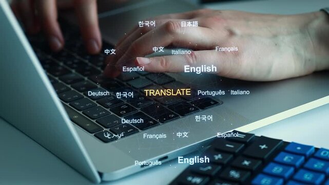People typing on a laptop keyboard while multiple languages appear on the screen in a bright workspace during daytime hours.