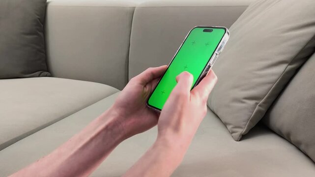 Hands hold smartphone with green screen and type message on mobile screen at home. Fingers write text on chroma interface. Concept communication, chatting, digital interaction, app usage..