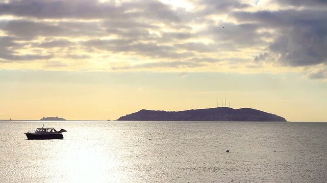 Soft pastel cloudy sunset over the sea near Kinali Island, Princes Islands, Istanbul, with a silhouetted yacht anchored offshore, its canopy flapping in the wind