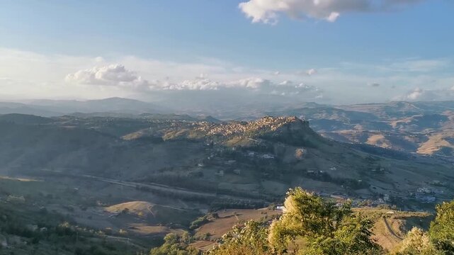 Scenic view of rolling hills and distant mountains under a vibrant sunset sky in Enna, Sicily, showcasing the natural beauty of the Italian landscape