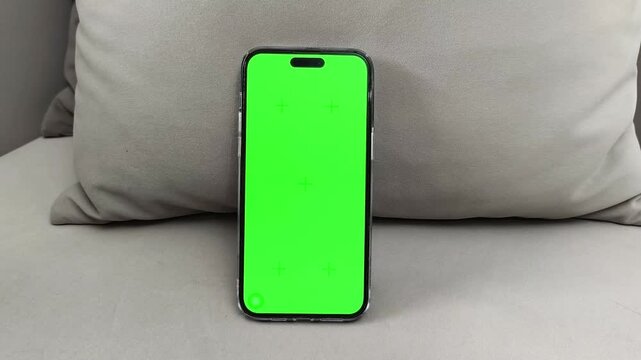 Close up smartphone with green screen on sofa and finger scrolls on display. Hand interacts with chroma interface using touch gesture. Concept app navigation, mobile browsing, digital