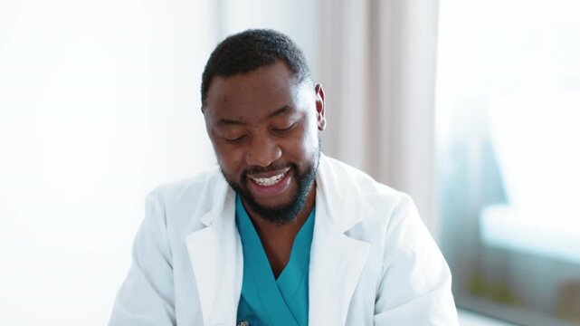 Telemedicine concept. Close up portrait of positive professional african american man doctor waving hand to camera and start talking, consulting patient online, slow motion