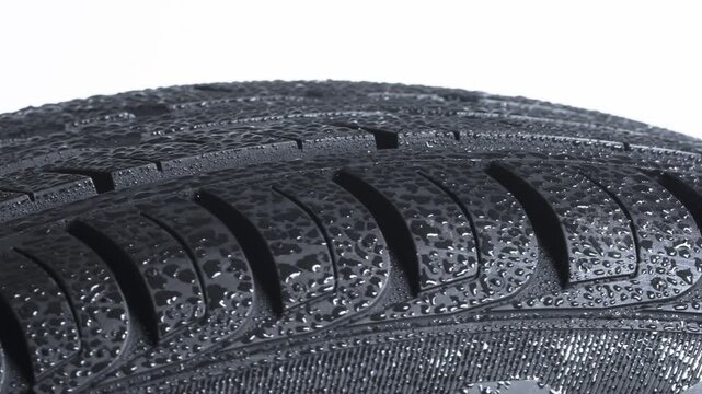 On a Car Tire Glittering Raindrops. Wet tire spinning on a white background close-up. It is covered with sparkling water drops