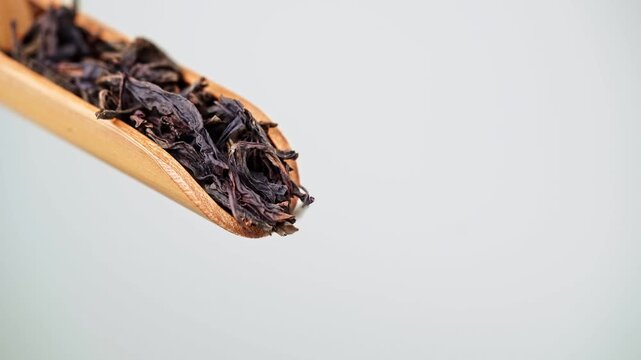 Macro Close-up of Premium Dried Black Tea Leaves Pouring from Wooden Scoop on Gray Background for Chinese Tea Culture Ads