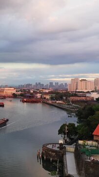 Wide view of the Pasig River with boats and the Manila skyline at sunset, featuring a mix of modern and historic architecture.