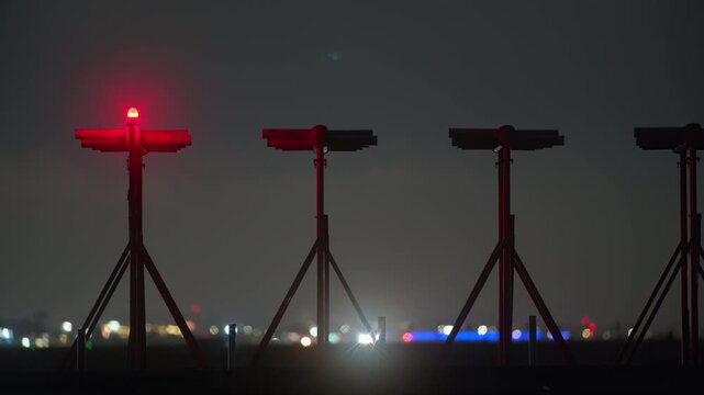 Row of approach lighting system towers with red beacon and airplane silhouette in distance