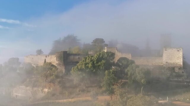 Lombardy Castle emerges from misty clouds, revealing ancient stone walls and lush greenery in Enna, Sicily, Italy, showcasing a captivating historical landscape
