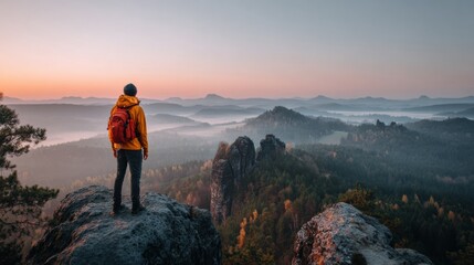 Fototapeta premium A traveler stands at a viewpoint with a backpack, gazing at the expansive landscape during golden hour light, surrounded by mountains and forests.