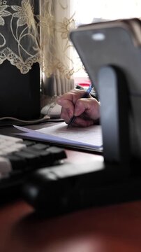 A close-up of the hand of a woman with nail dystrophy writing with a pen in a notebook while sitting at a table.