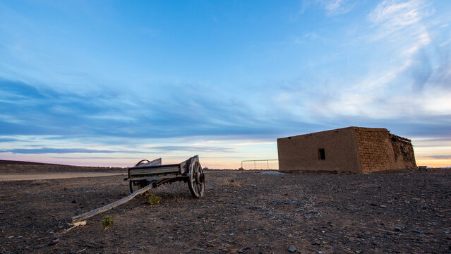Old ox wagon near abandoned dwelling in the Tankwa Karoo National Park at sunset with clouds in the sky