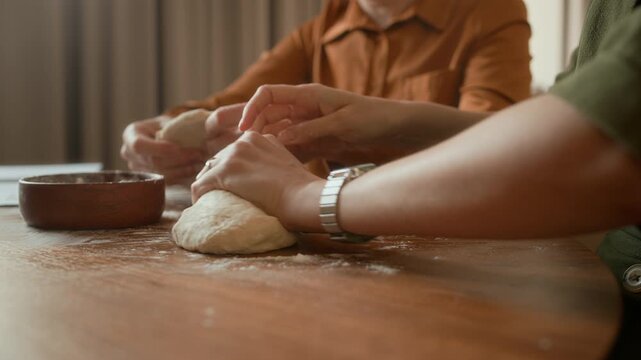 Cropped shot of hands of unrecognizable people kneading dough on wooden table while cooking together at home