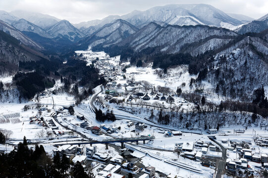 Aerial view from Risshaku-ji Buddhist Temple on the mountainside overlooking Yamadera village in the valley & a train of  Senzan Railway traveling on a bridge in snowy winter season in Yamagata, Japan
