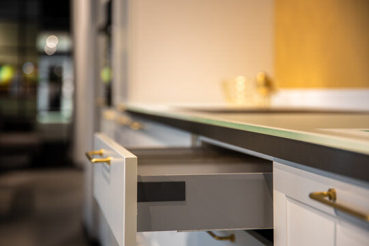 Open kitchen drawer in modern interior close up. Minimal white cabinetry with gold handles.