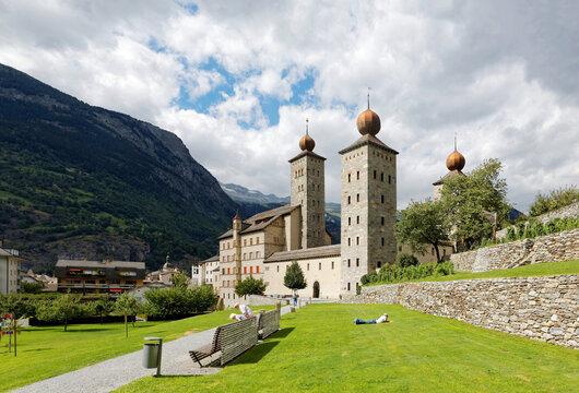 Scenery of historic Stockalper Palace with towers of gilded onion domes and a tourist basking in the sun on the green grassy meadows on a sunny cloudy summer day, in Brig-Glis, Valais Switzerland