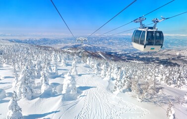 A scenic cable car flying over a piste in Zao hot spring and ski resort, with Juhyo forest (ice trees or snow monsters) all over the slope under blue clear sky on a sunny winter day in Yamagata, Japan © AaronPlayStation
