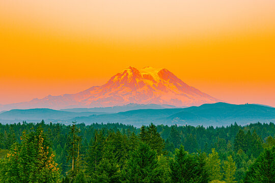 Iconic Mount Rainier bathed in intense orange and pink sunset colors with layered ridges in the foreground.