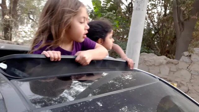 Authentic UGC clip of three happy little girls looking out of moving car sunroof making funny faces