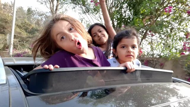 Authentic UGC clip of three happy little girls looking out of moving car sunroof making funny faces