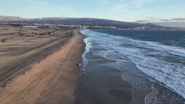 Drone flight along beach shoreline with gentle waves and walking people, no LUT, 60 fps