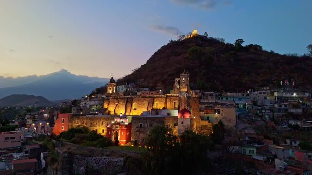 Aerial night view of illuminated colonial cathedral and hilltop church in Atlixco, Puebla, Mexico