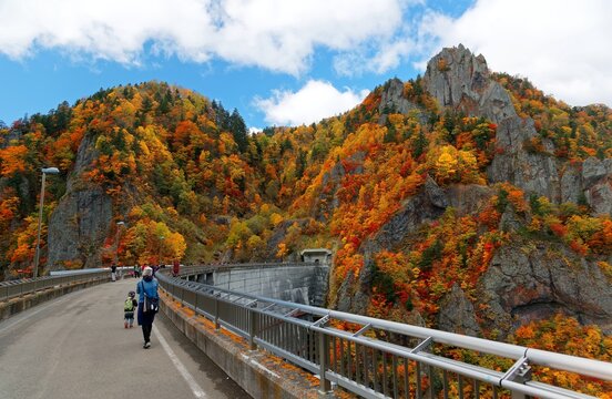 Tourists enjoying vibrant fall colors on the rocky cliffs by Hoheikyo Dam, a reservoir in a beautiful gorge under environmental protection in Shikotsu-Toya National Park in Sapporo, Hokkaido, Japan