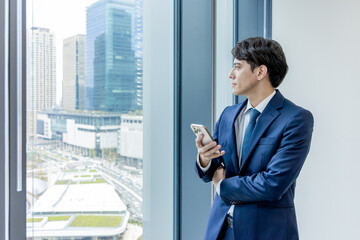 Fototapeta premium ビル背景が綺麗なオフィスでスマートフォンを使うビジネスマン
