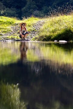 Young girl with hat snorting drops by stream. Woman playing in nature with flowing water in river.
