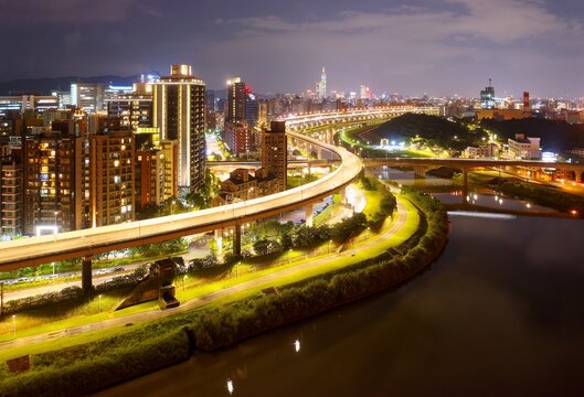 Aerial view of HuanDong Boulevard, an elevated expressway along Keelung River in Nangang, Taipei City, with 101 Tower standing among crowded buildings in Xinyi District & city lights dazzling at night