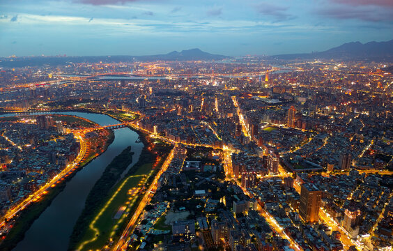 Aerial night skyline of Taipei City, with a view of Xindian River winding thru downtown, 101 Tower standing out amid crowded buildings in Xinyi Commercial District and city lights glowing at blue dusk