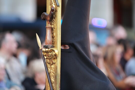 Black-hooded Nazareno beside gilded processional standard during Holy Week in Madrid, Spain
