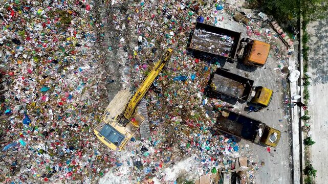 Aerial view of landfill site with excavator and trucks handling large scale garbage waste and pollution
