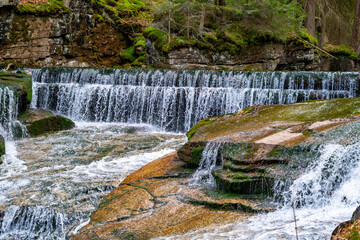 Picturesque waterfall on mountain stream flowing in cascades over granite rocks in forest, crystal clear water, green moss on stones, wild nature landscape, river flow in mountains, scenic outdoor vie © Adam