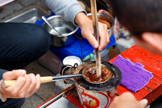 A street vendor stirring melted sugar in a ladle over a charcoal stove to make crispy Pong Tang Candy, a retro dessert and local people's nostalgic childhood snack, in Anping Old Town, Tainan, Taiwan