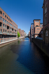 Naklejka premium Historic brick buildings along canal in Hamburg Speicherstadt with calm water and blue sky.
