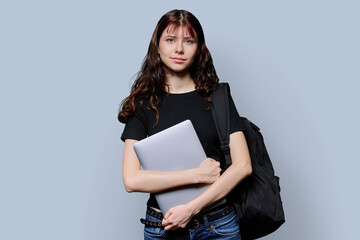 Portrait of beautiful girl teenage student with backpack, laptop on gray background
