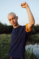Obraz premium Young man raising fist near riverbank in outdoor park on warm evening