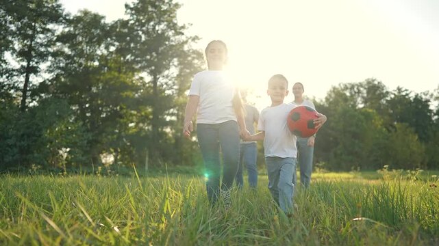 Happy family walk in park. Father and children holding hand while boy carries red soccer ball. Family enjoying outdoor playtime together. Family connection with father park. Children smiling in park.