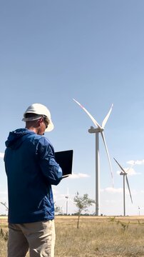 Worker inspects windmill renewable energy farm. Windmill worker ensures industry standards clean environment. Industry worker monitors windmill performance. wind energy industry protecting environment