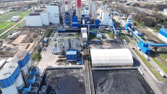 Aerial view of industrial enterprise showing continuous operation of machinery on a coal storage site with surrounding buildings, roads, and rail tracks in a bustling urban landscape
