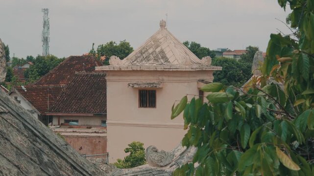 A scenic view overlooking the ancient terracotta tiled roofs and a historic bell tower of the Keraton Yogyakarta palace complex during a peaceful, cloudy afternoon in Indonesia.