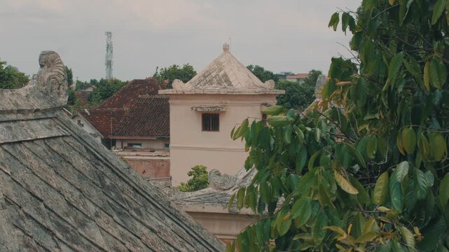 A serene architectural landscape featuring weathered clay tile roofs and a historic tower building in Indonesia, captured during daylight with soft atmospheric lighting.