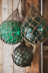 Handcrafted vintage Japanese glass fishing floats in decorative twine netting, hanging against a rustic wooden wall. Authentic maritime decor featuring aged sea glass orbs with weathered textures. © Francis