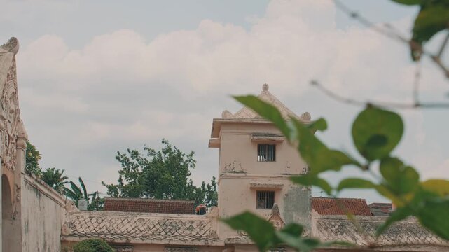 A low-angle cinematic shot of a weathered stone palace structure in Yogyakarta, featuring traditional roof tiles and colonial influence under a soft, golden hour sky.