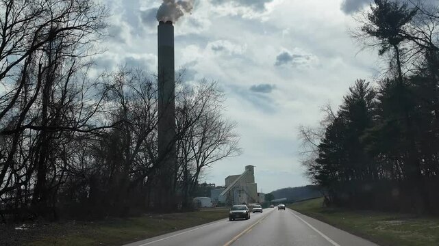 Driving Past a Tall Smokestack on a Cloudy Day Near a Road