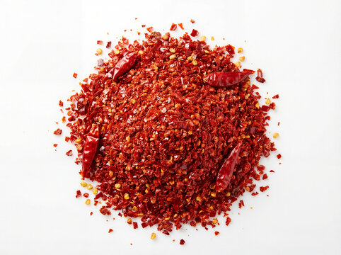 Crushed red chili pepper flakes and whole dried peppers pile isolated on white background for culinary seasoning