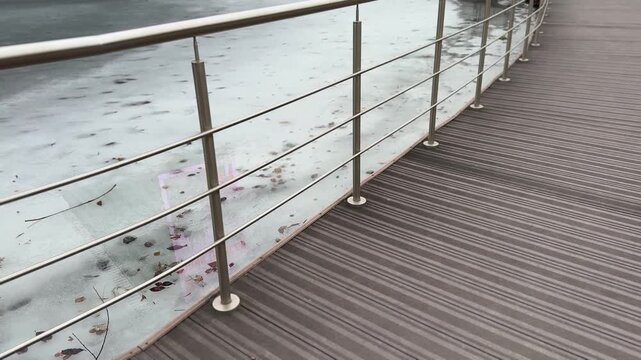 Icy reservoir jetty with steel railings, textured boardwalk and thin shore ice, overcast sky and muted tones, industrial detail.