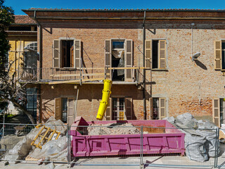 Fototapeta premium Construction site for the renovation of an old residential building. A yellow debris chute conveys the rubble into a roll-off container positioned at street level